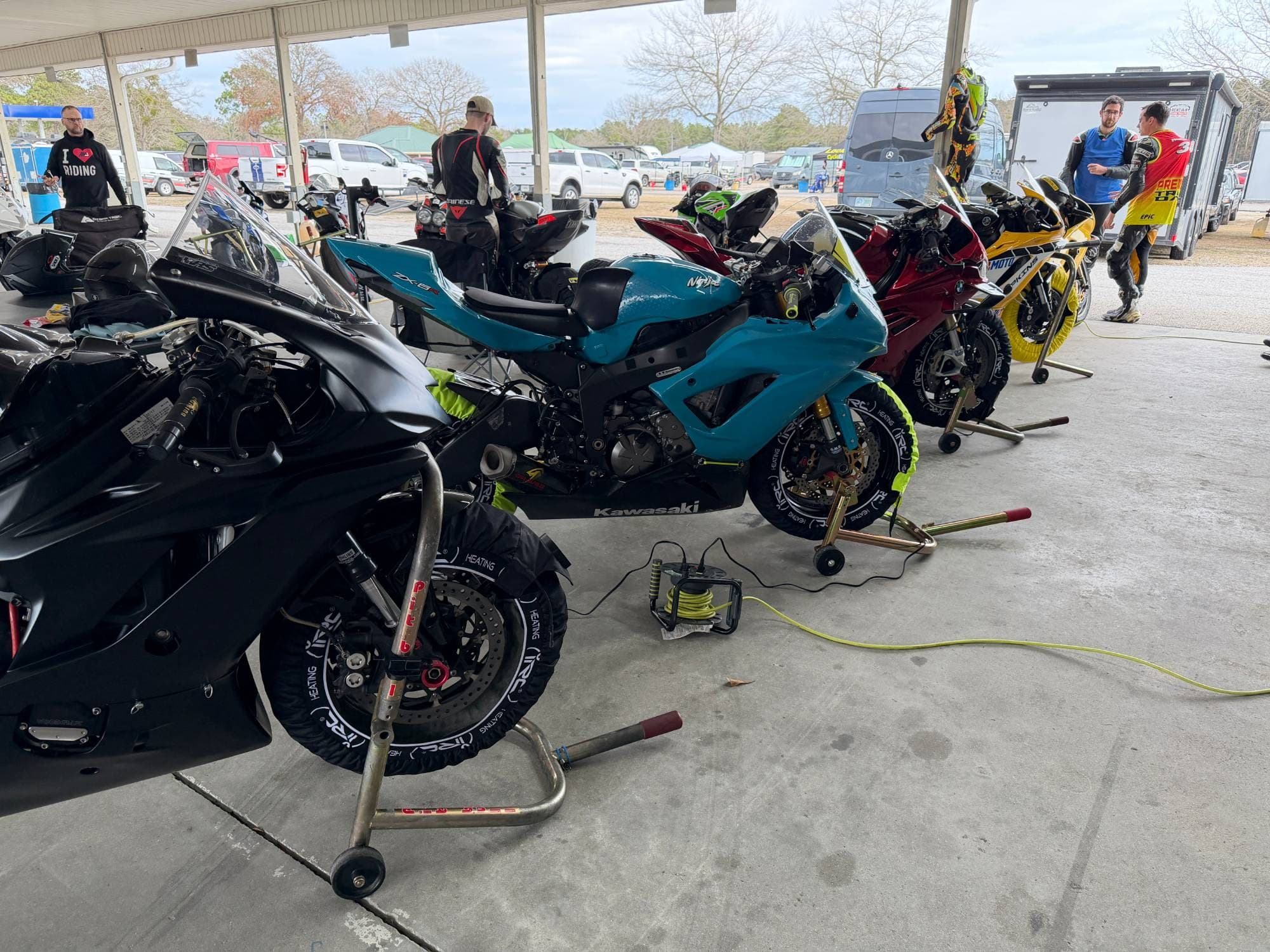 Row of track bikes on IRC Components tire warmers under a paddock awning