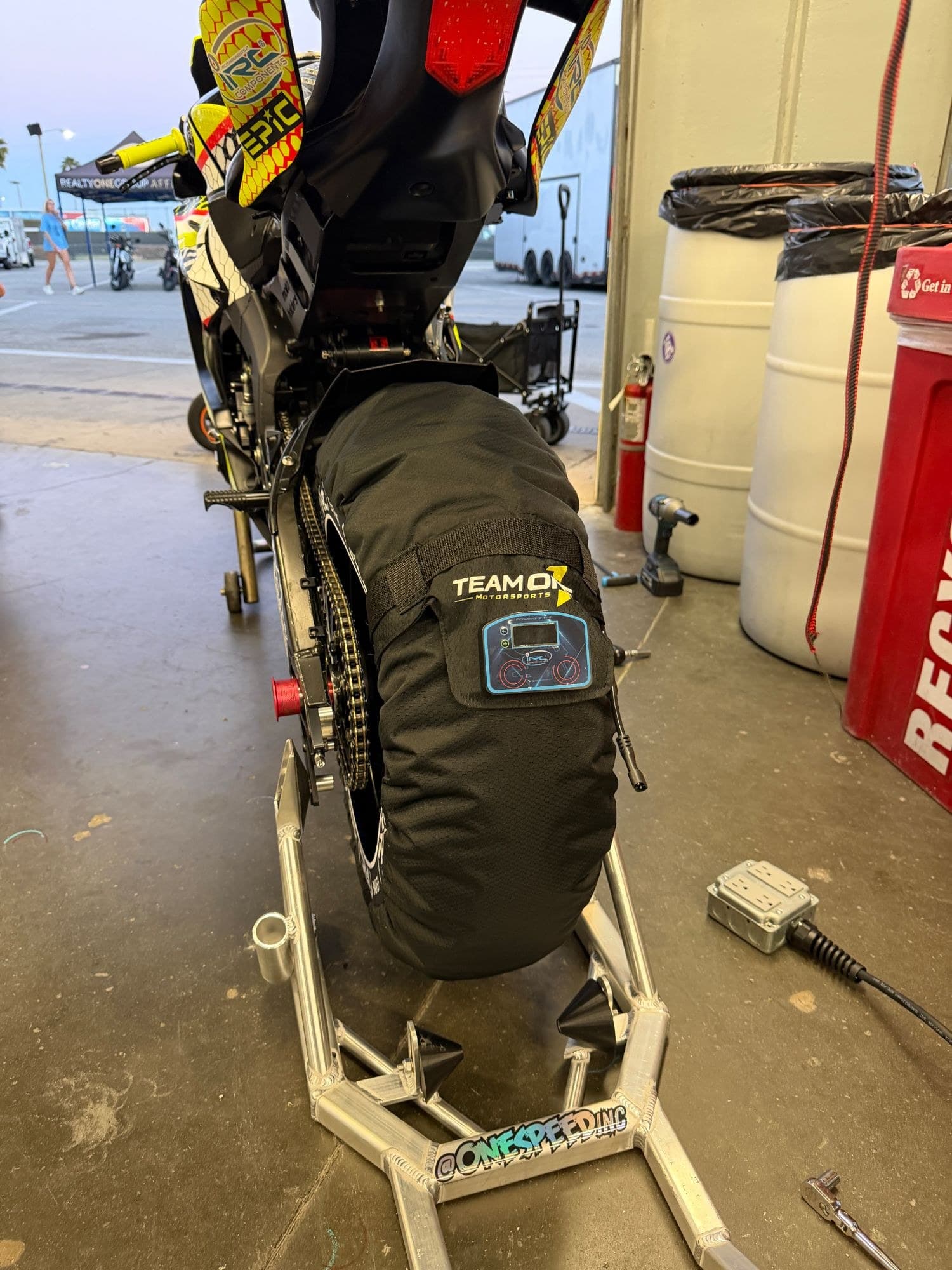 Team One Motorsports branded IRC tire warmer heating a rear slick on a paddock stand